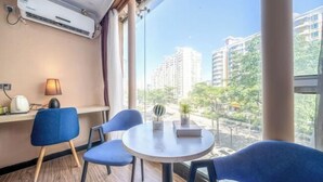 A hotel room with a round table, two blue chairs, a lamp, and a view of tall buildings and greenery outside. - 8 Inn (Shenzhen)