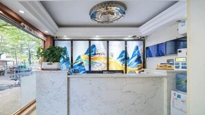 A reception area with a marble counter, a potted plant, a large window, and a wall-mounted television. - 8 Inn (Shenzhen)