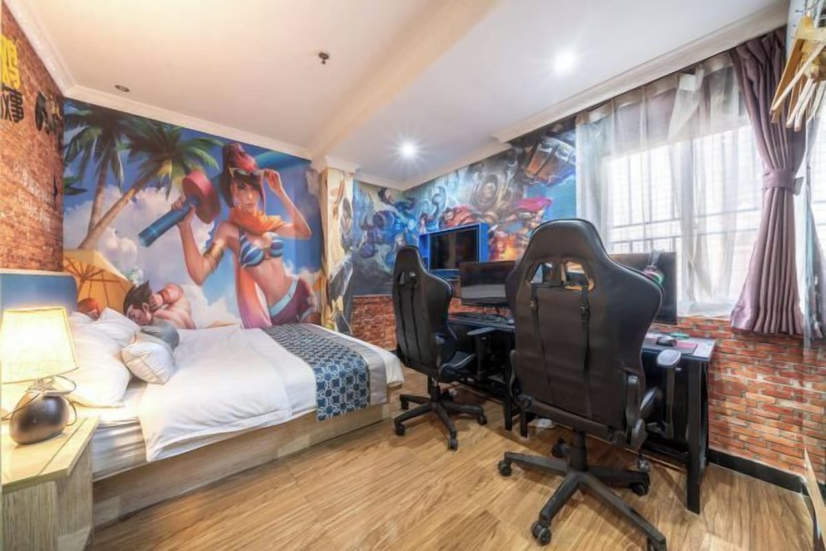 A bedroom with a bed, a desk, two chairs, a TV, and a mural on the wall.