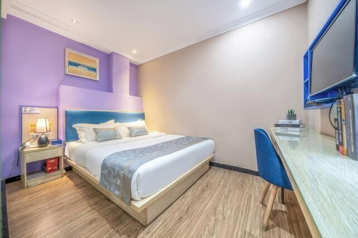 A hotel room with a bed, a desk, a chair, a nightstand, and a television.