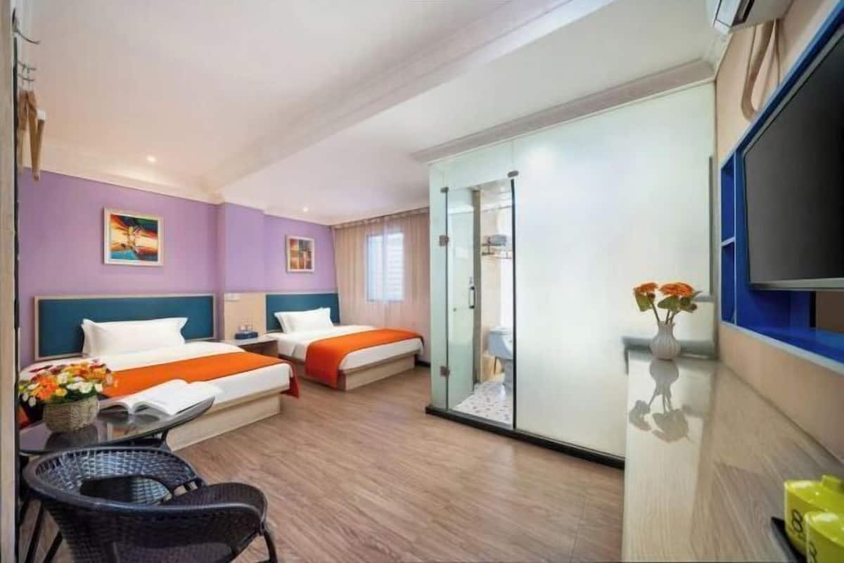 A hotel room with two beds, a glass partition, a television, and a small table with flowers.