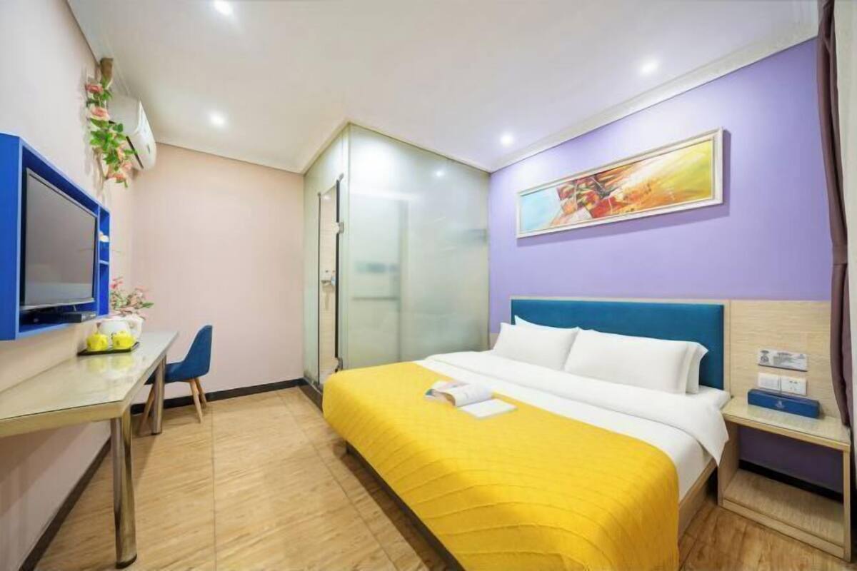 A hotel room with a bed, a desk, a chair, a TV, and a painting on the wall.