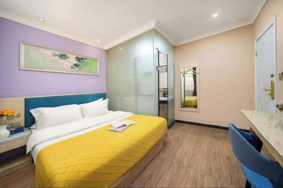 A hotel room with a bed, bedside table, and a mirror.