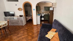Un espace de vie compact comprenant un canapé, une table à manger, un téléviseur et une kitchenette.