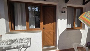 Un bâtiment blanc avec une porte et des fenêtres en bois, un étendoir et un parasol rayé.