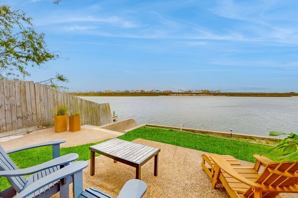 A patio with Adirondack chairs, a wooden table, and a view of a body of water.