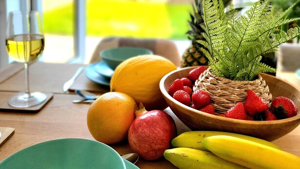 A dining table with a fruit bowl, plates, and a glass of white wine. - Seaside beach themed home with garden and driveway (Lytham St Annes)