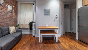 A compact living space with a grey sofa, a wooden table, a radiator, and a grey refrigerator. - Lovely 2 bedroom Central Manhattan (New York)