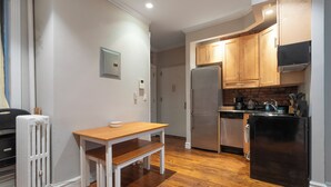 A compact kitchen with wooden cabinets, a stainless steel refrigerator, and a dining area with a wooden table and bench. - Lovely 2 bedroom Central Manhattan (New York)