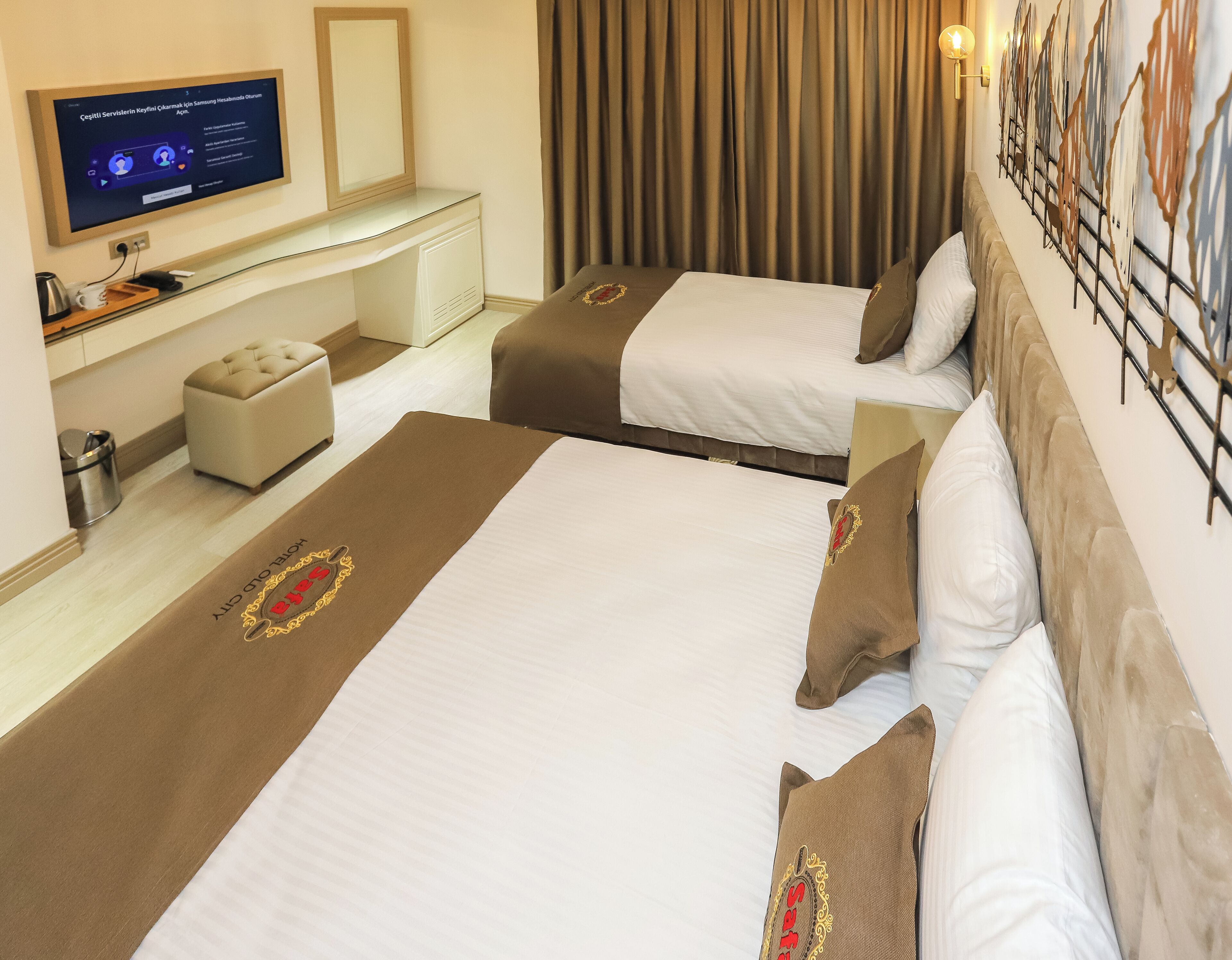 A hotel room with two beds, a TV mounted on the wall, a desk, and a curtain.