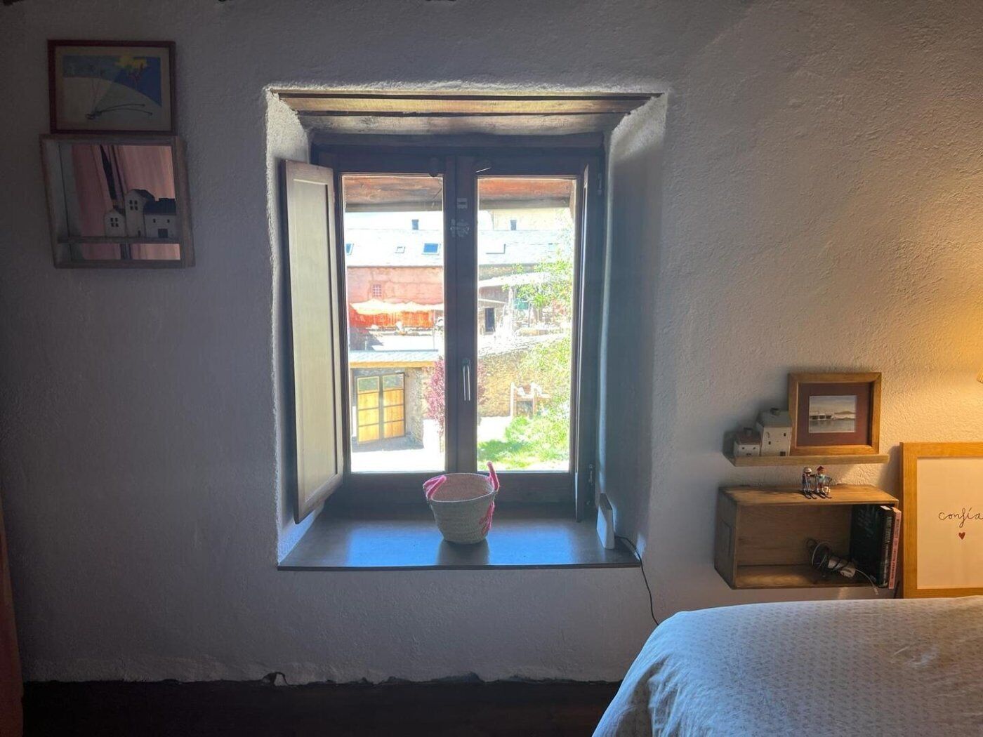 Une pièce avec une fenêtre, un lit et une étagère contenant des livres et un tableau encadré.