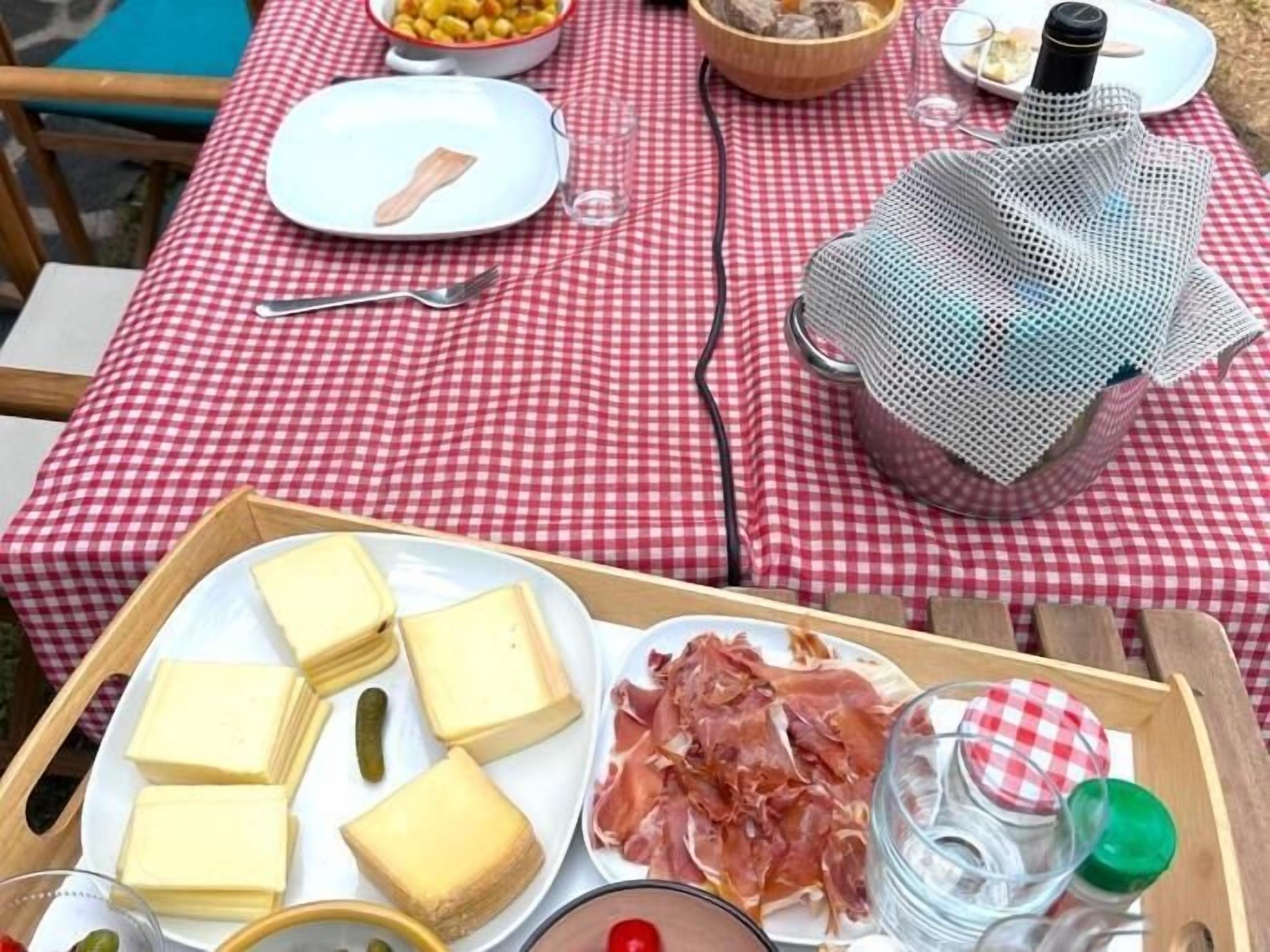 A picnic setup with a checkered tablecloth, a tray with cheese, cured meats, and condiments.