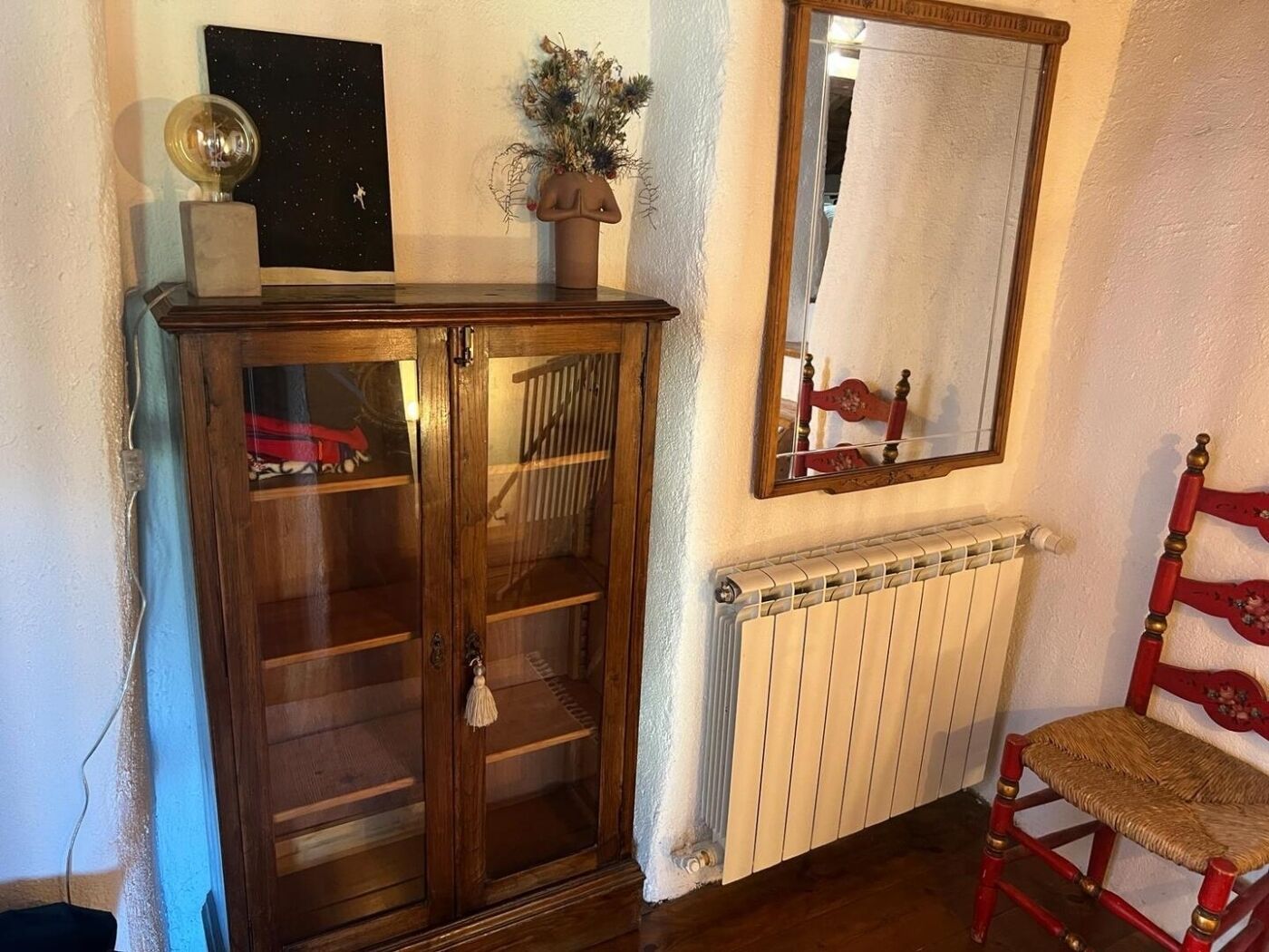 Een houten kast met glazen deuren, een spiegel, een radiator en een rode stoel.