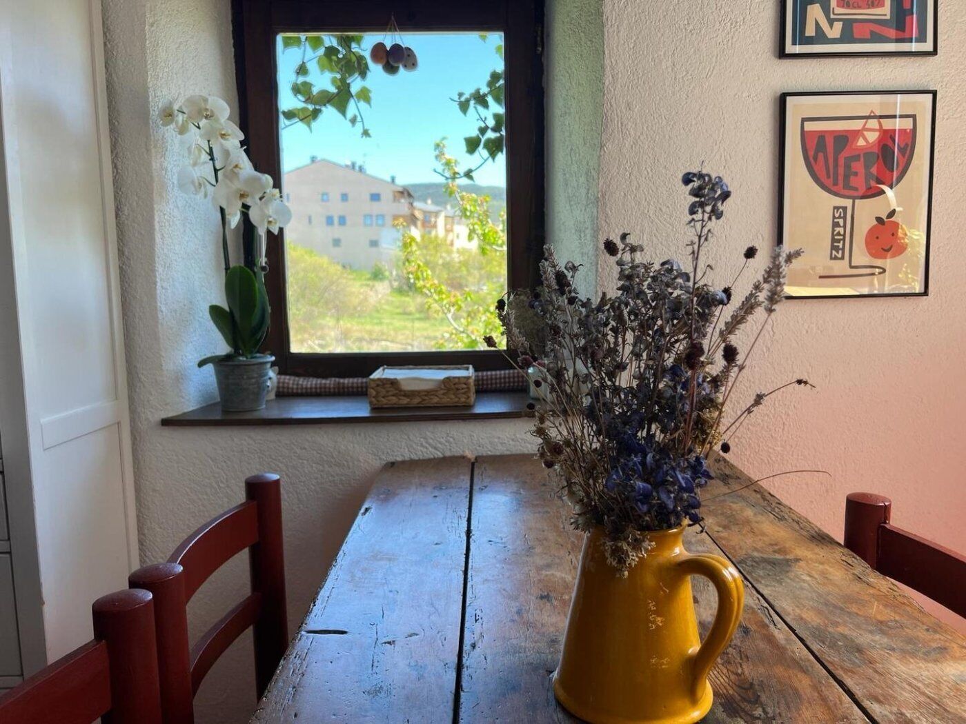 A wooden table with a yellow vase of dried flowers and a potted plant with white flowers.