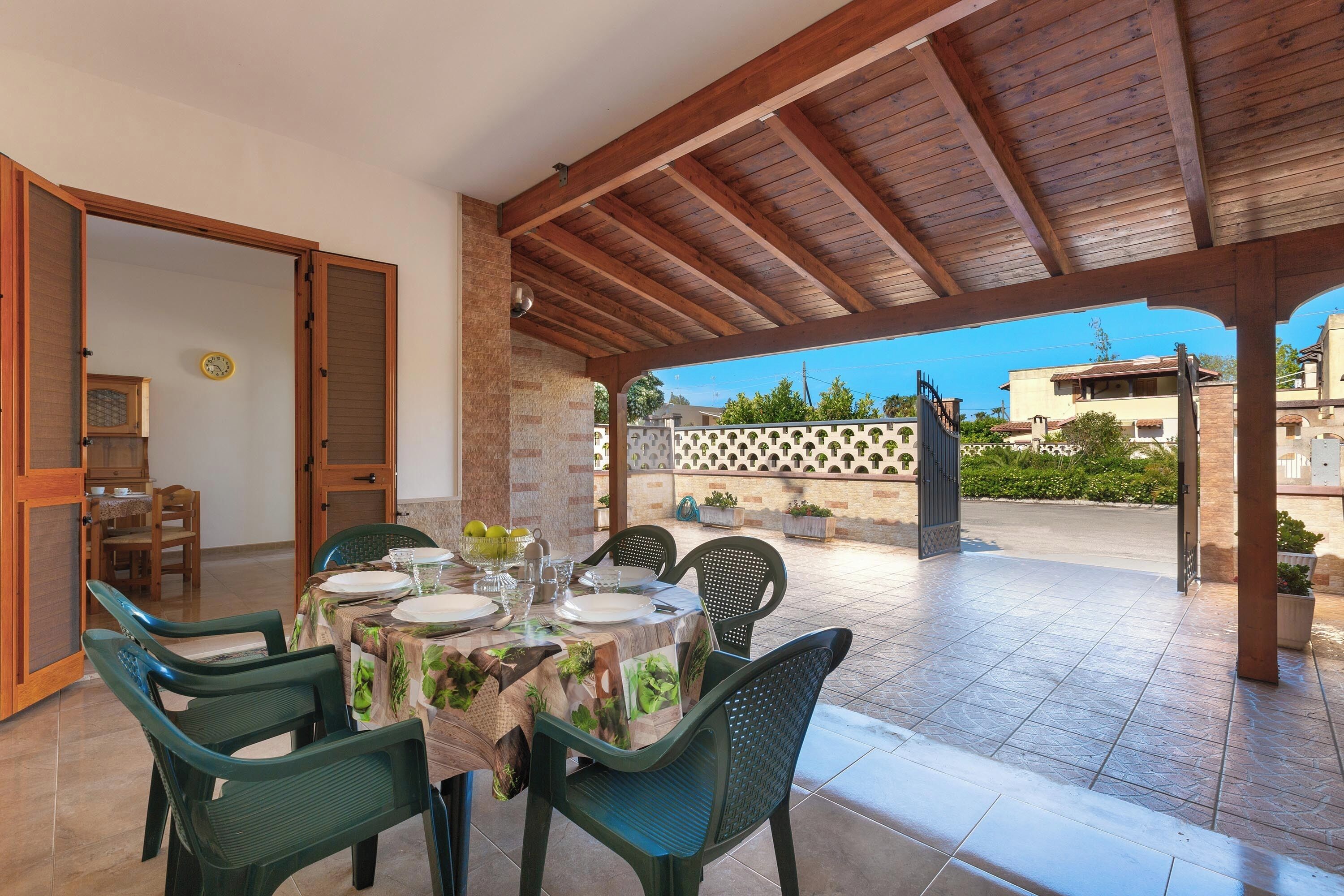 An outdoor patio with a wooden pergola, a table set for dining, and chairs.