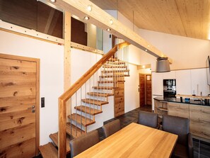 A modern kitchen with a wooden staircase, a dining area with a wooden table, and a kitchen island.