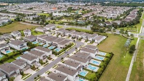 An aerial view of a residential area with houses arranged in a grid pattern, featuring green lawns and swimming pools.