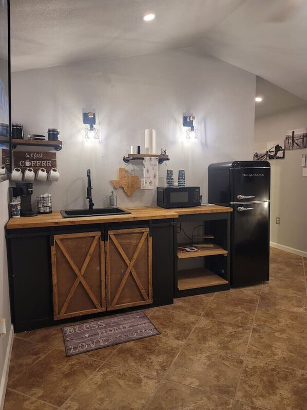Cocina compacta con encimera de madera, refrigerador negro y una estación de café.