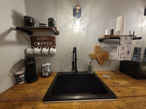 Una cocina con un lavabo negro, cafetera y estantes con recipientes de café y un mapa de Texas.