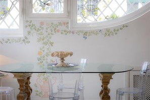 Un comedor con una mesa de vidrio, sillas transparentes y una pared decorativa con motivos florales.