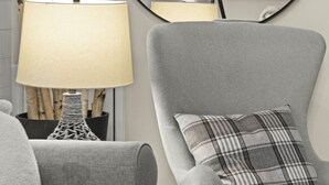 Una sala de estar moderna con un sillón gris, un espejo redondo y una lámpara.