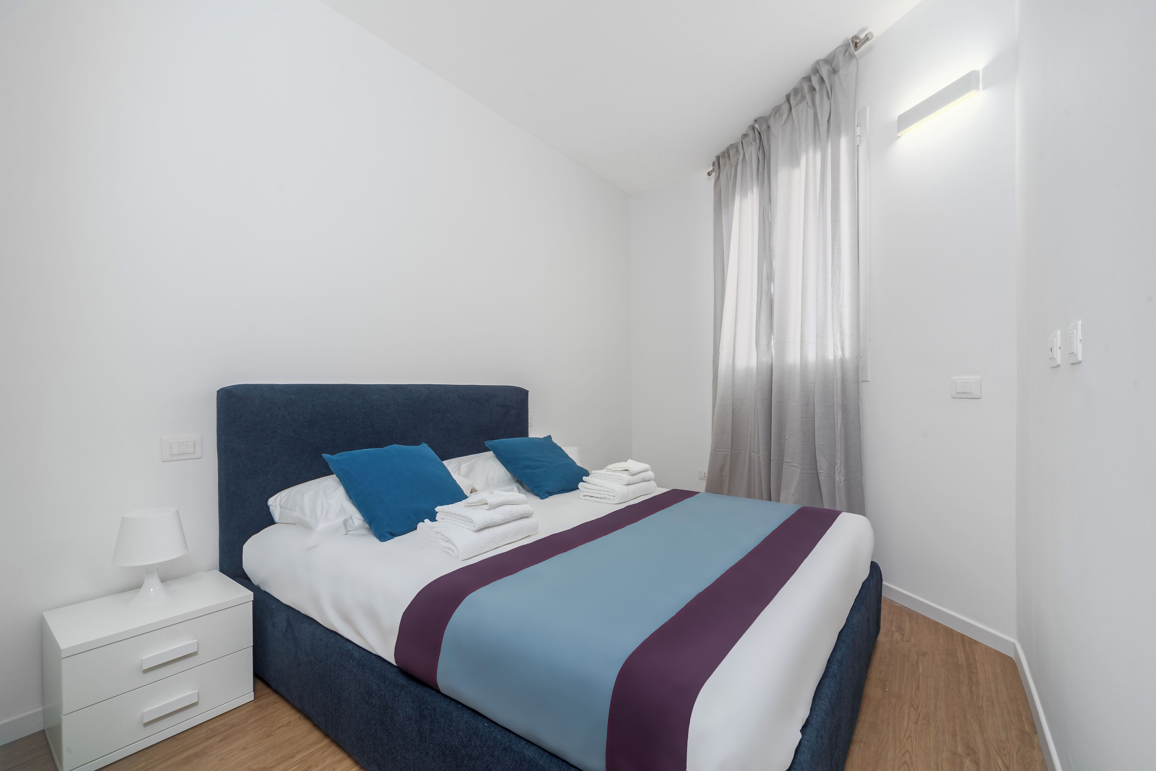 A neatly made bed with a blue headboard, white bedding, and a purple accent.