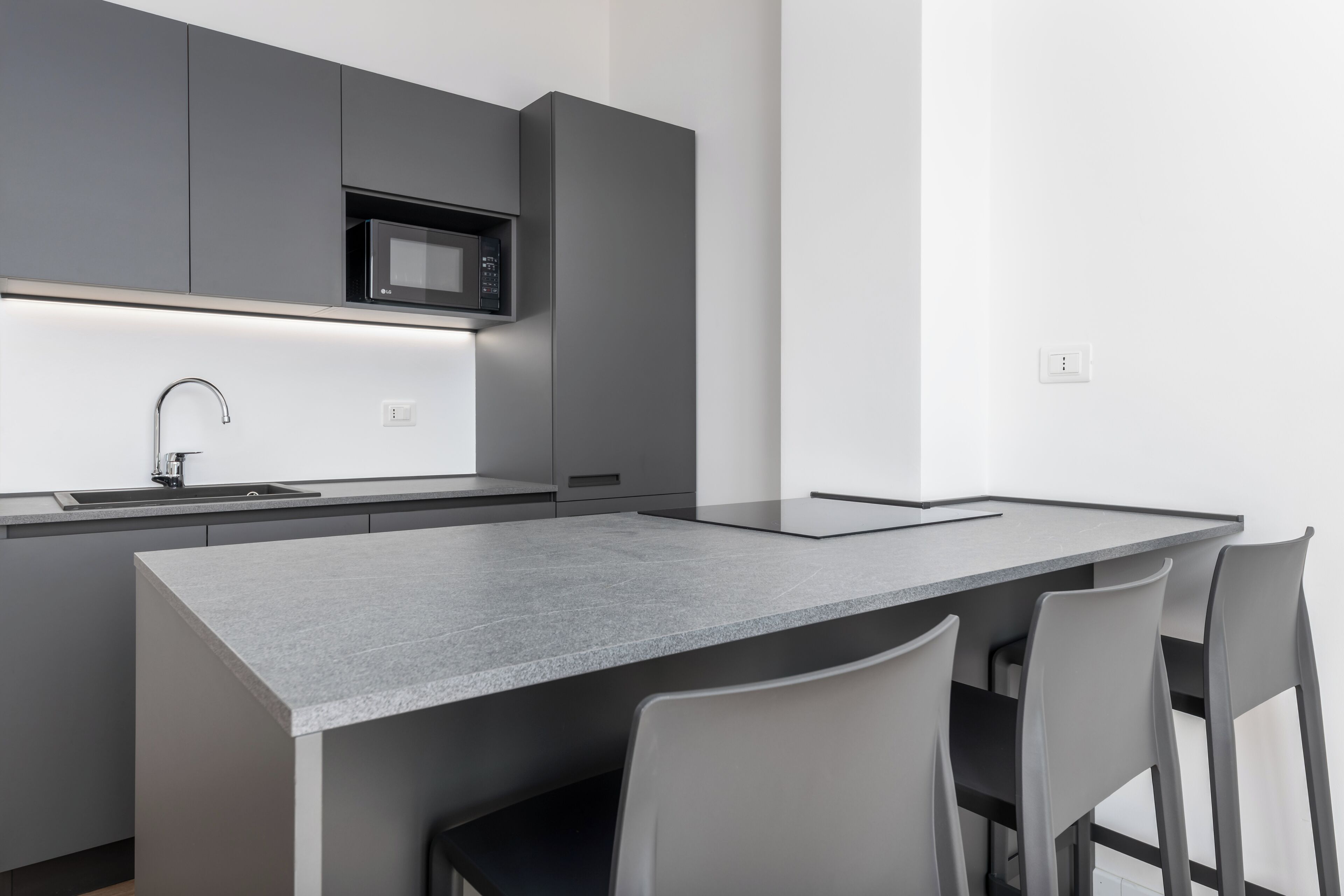 Una cocina moderna con armarios grises, microondas integrado, pileta de acero inoxidable y una isla grande con sillas.