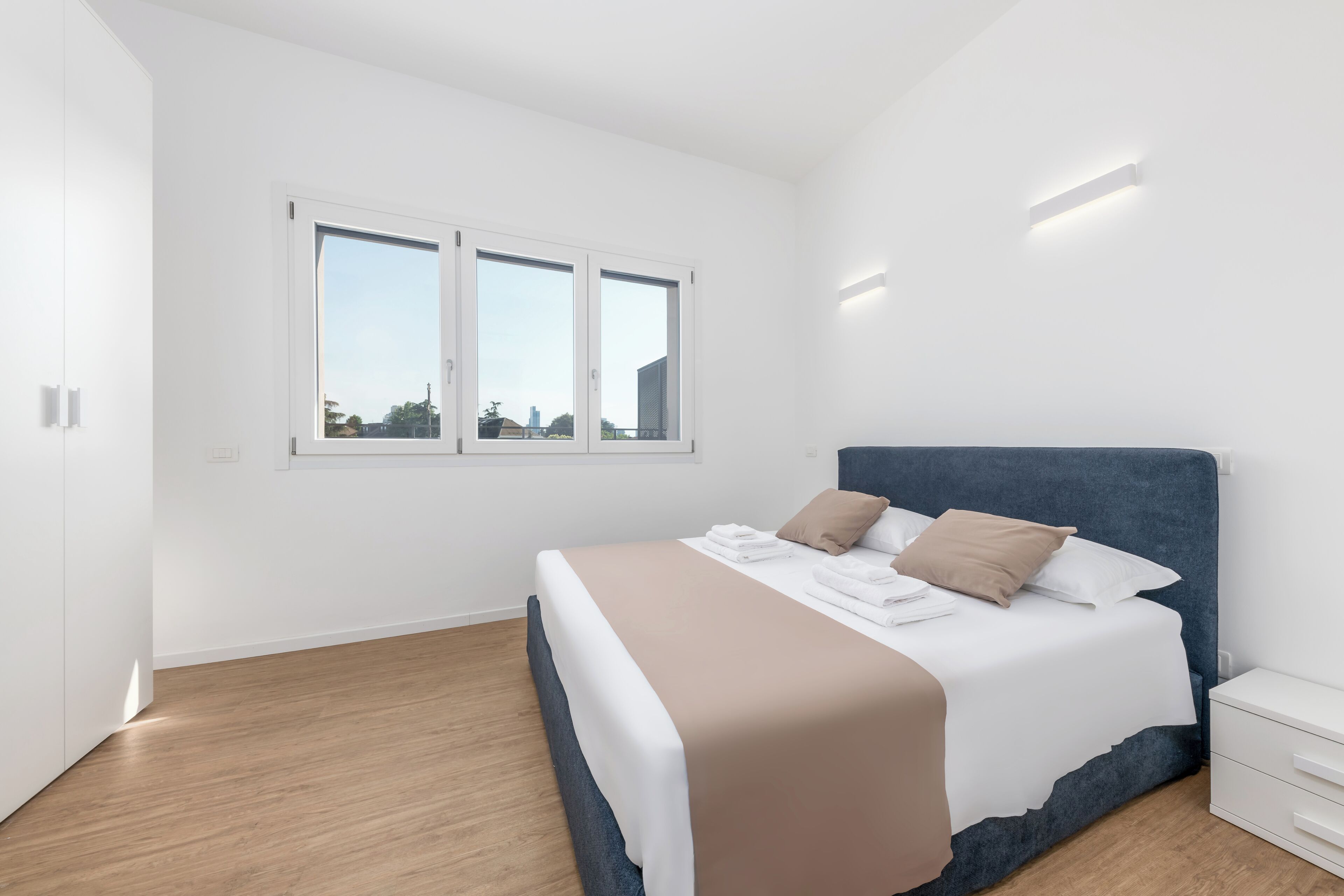 A modern bedroom with a large bed, white walls, and a wooden floor.