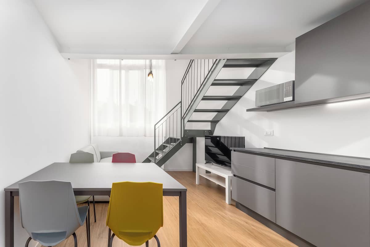 A modern kitchen with stainless steel appliances, a wooden floor, and a staircase leading to a loft area.