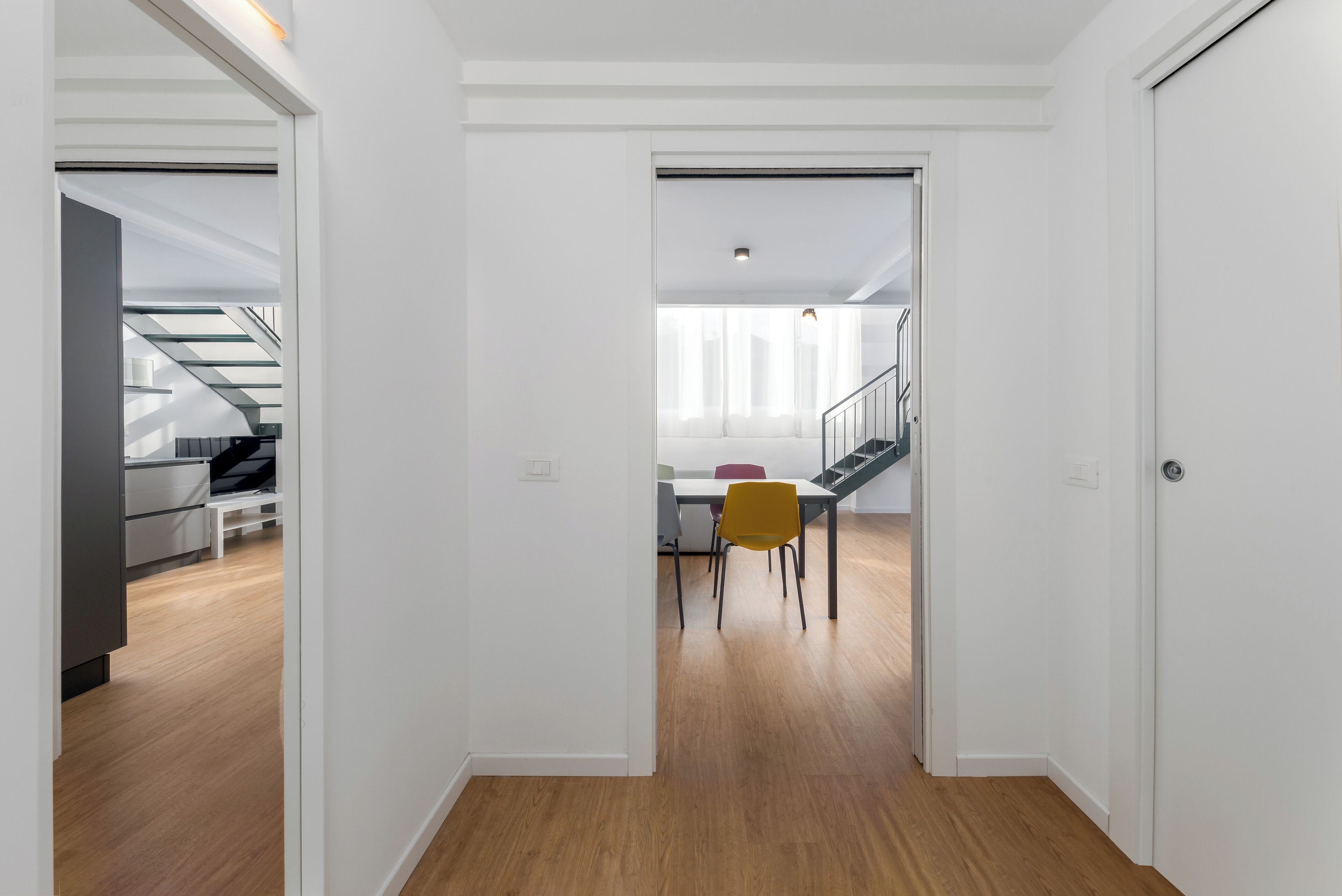Un interno moderno con pavimento in legno, pareti bianche e un'area pranzo con una sedia gialla.