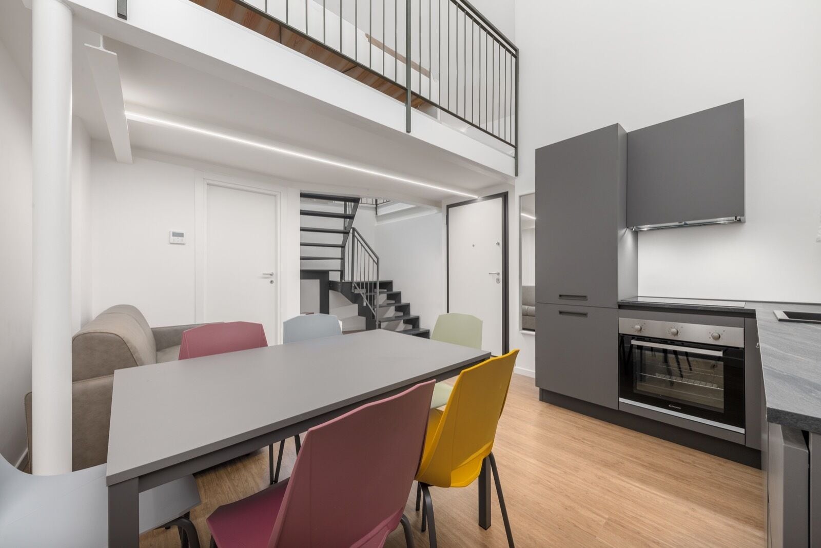 A modern kitchen with a dining area, a staircase, and a built-in oven.