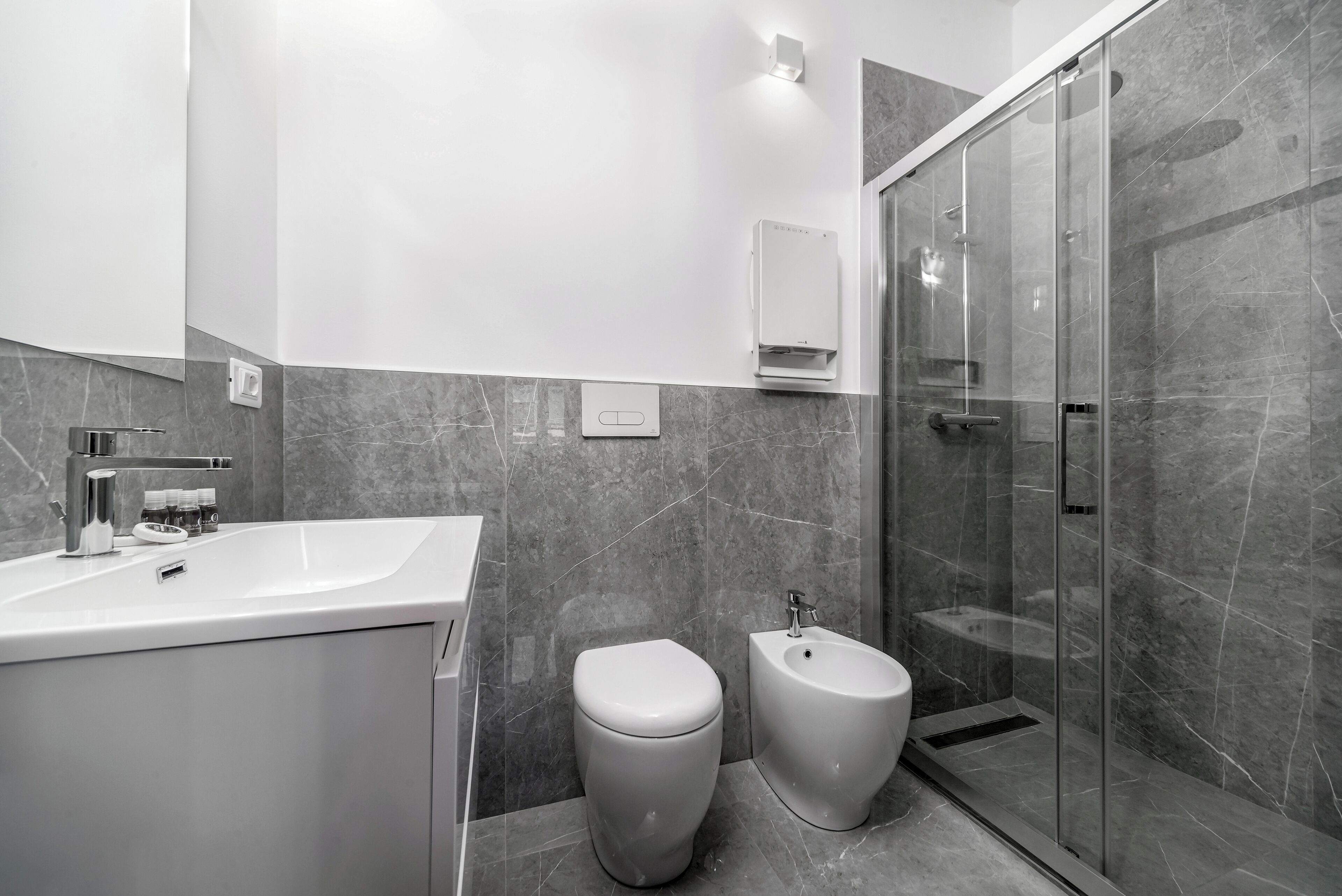 A modern bathroom with a large sink, toilet, bidet, and glass-enclosed shower.