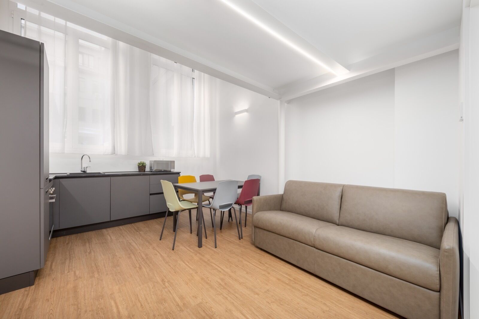 Una cocina moderna con comedor, sofá y ventana con cortinas traslúcidas.
