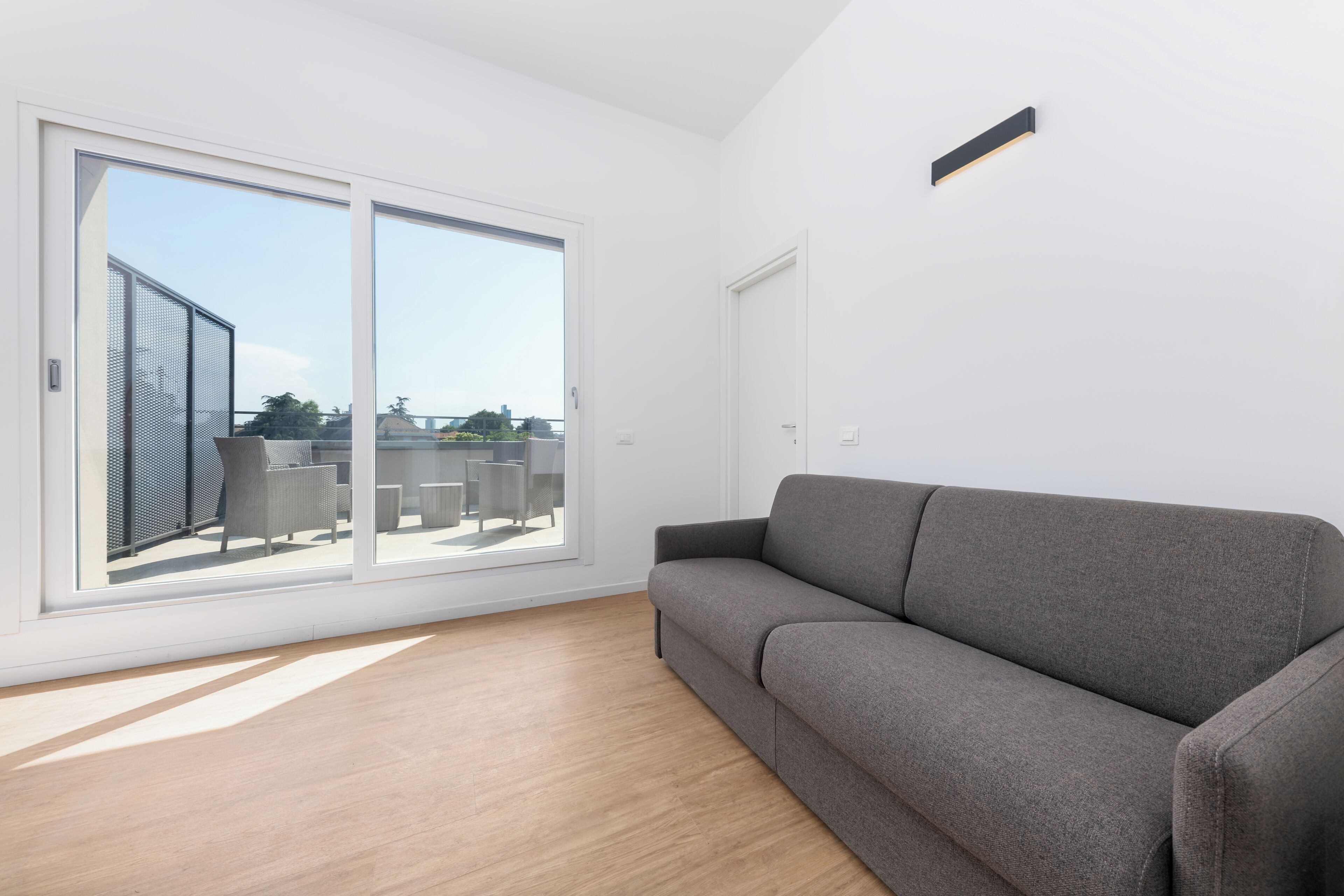 Un salón moderno con un sofá gris, grandes puertas correderas de vidrio y vistas al exterior.