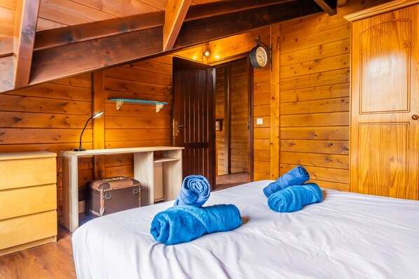 A wooden cabin room with a bed, a desk, and a suitcase.