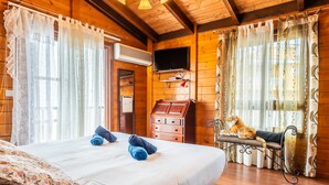 Habitación tipo cabaña de madera con cama, televisor, un pequeño mueble de madera y un tigre en un banco.