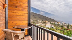 Un balcón con mobiliario de mimbre, vista a un pueblo costero y una pared de madera.