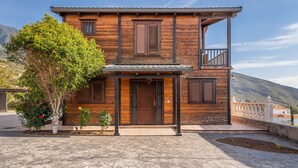 Una casa de madera de dos pisos, con balcón, entrada empedrada y un árbol en primer plano.