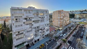 A multi-story residential building with balconies, a parking area, and a clear sky.