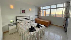 A bedroom with a bed, bedside tables, a small table with a towel, and a window with a view of buildings.