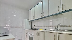 A kitchen with white cabinets, a stove, a sink, and a microwave. - TERRASOL FAROMAR 4 (Torre del Mar)