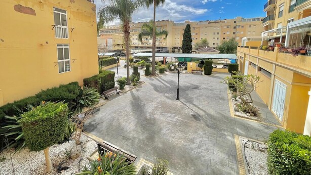 A courtyard with a paved area, palm trees, and a building with balconies. - TERRASOL FAROMAR 4 (Torre del Mar)