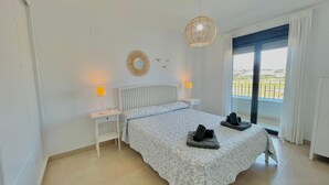 A bedroom with a large bed, two bedside tables with lamps, a large window with a view, and a hanging light fixture. - TERRASOL AZUCARERA 4 (Torre del Mar)