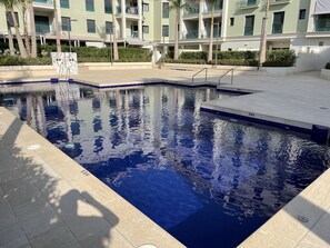 A swimming pool with clear blue water, surrounded by a tiled deck and palm trees. - TERRASOL AZUCARERA 4 (Torre del Mar)