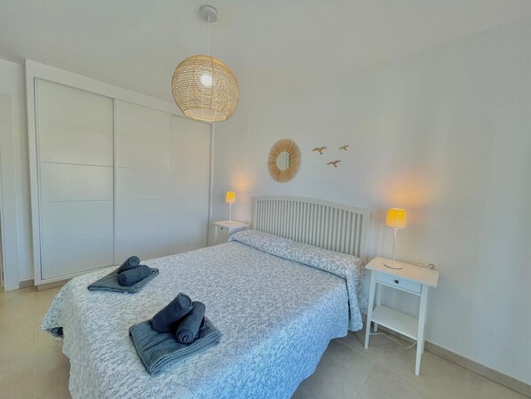 A bedroom with a bed, two bedside tables, a hanging light fixture, a wardrobe, and wall decorations. - TERRASOL AZUCARERA 4 (Torre del Mar)