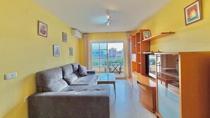 Una sala de estar con sofá, televisión y balcón con mesa y sillas.