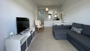Una sala moderna con un sofá gris, un televisor y un mueble blanco para entretenimiento.