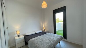 Un dormitorio con cama, mesitas de noche, una lámpara colgante y un ventanal grande.