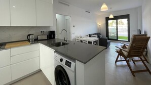 Una cocina moderna con lavadora integrada, un comedor con mesa y sillas, y un amplio ventanal corredero que da a un balcón.