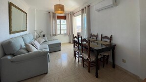 Un saló amb un sofà, una taula de dinar amb cadires, una làmpada penjant i una finestra amb cortines.